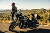 Side angle of a person standing next to a parked motorcycle.